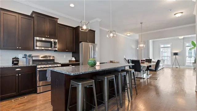 a kitchen with stainless steel appliances granite countertop a stove top oven a sink dishwasher a dining table and chairs with wooden floor