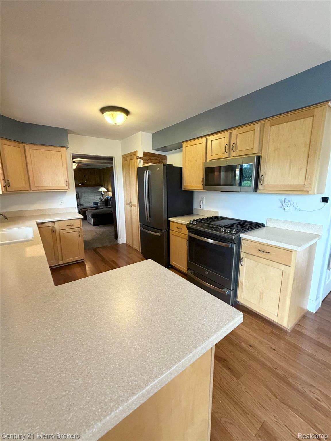 3259 North Seymour Road Flushing, MI 48433 - Photo 22 of 49 Kitchen featuring wood-finish flooring, light wood cabinetry, speckled countertops, and stainless steel appliances including a refrigerator, range, and microwave