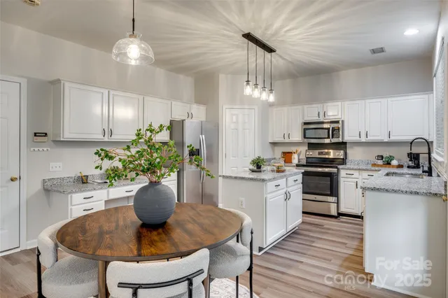 a kitchen with stainless steel appliances granite countertop a dining table chairs refrigerator and cabinets