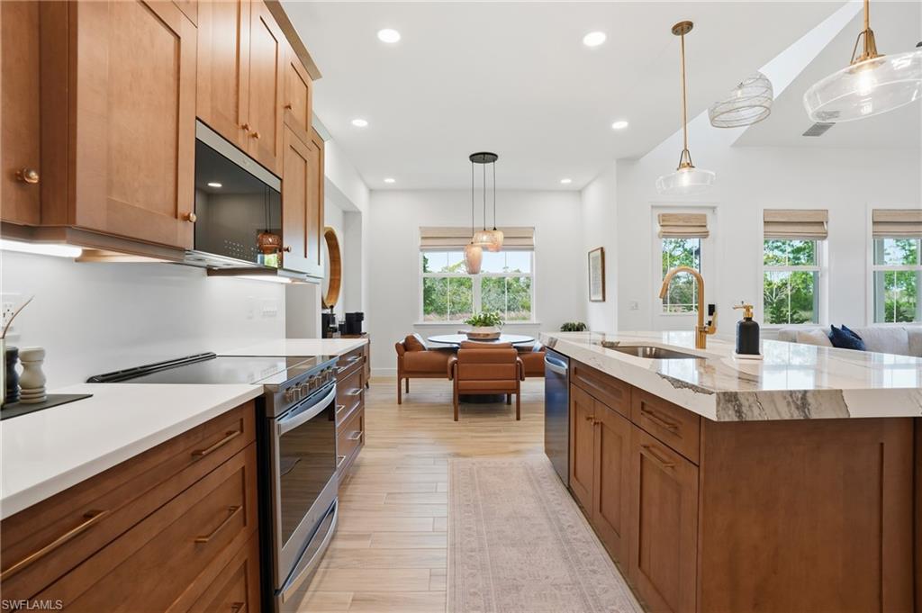 6975 Saona Court Naples, FL 34113 - Photo 9 of 30 a kitchen with stainless steel appliances a sink dishwasher a stove a microwave oven and a dining table with wooden floor
