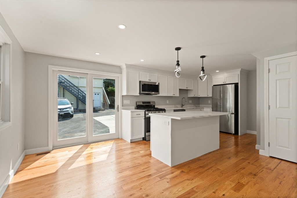 80 Newhall Street Lynn, MA 01902 - Photo 3 of 16 a large kitchen with kitchen island a sink a stove a refrigerator and white cabinets with wooden floor