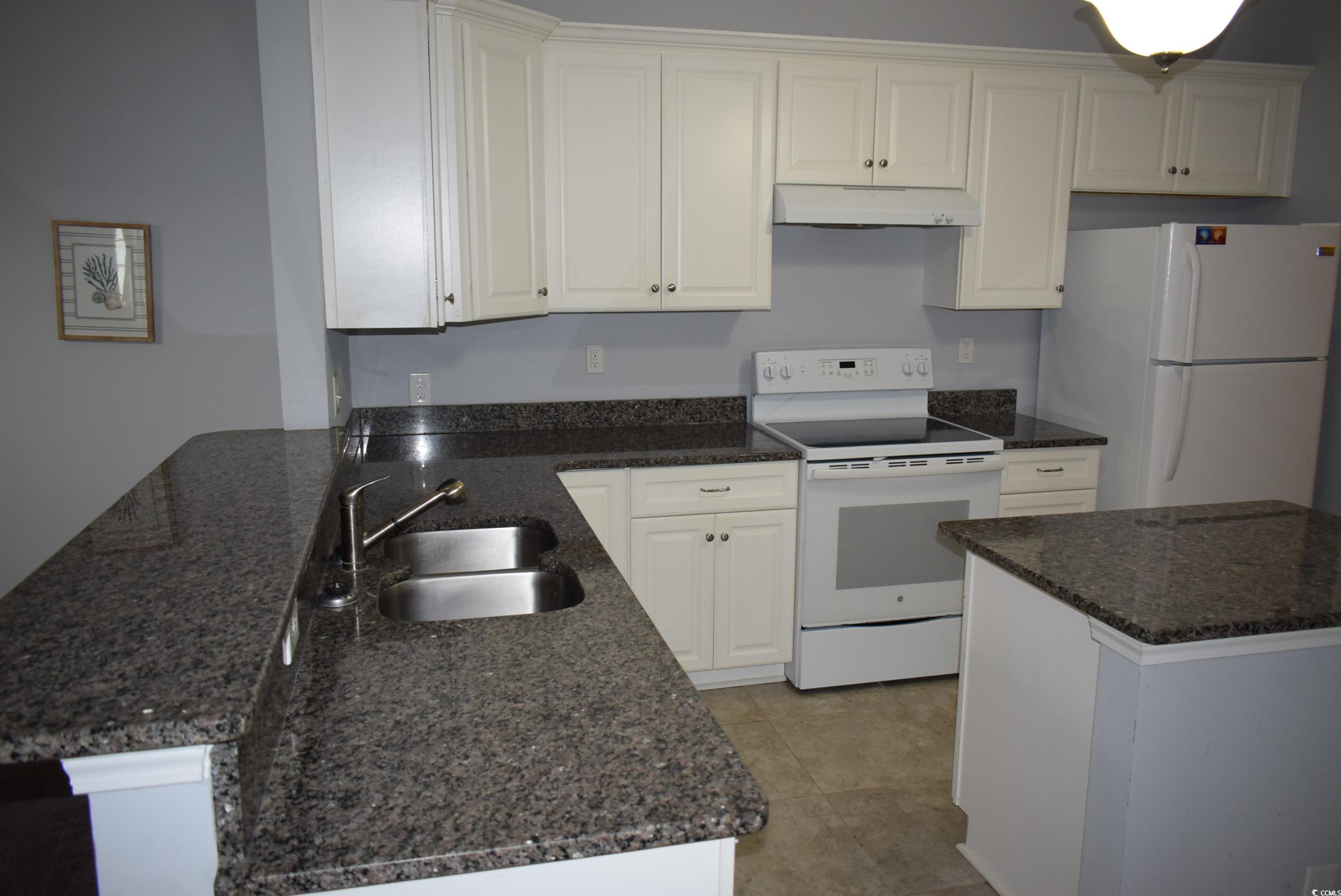 216 Rose Water Loop Myrtle Beach, SC 29588 - Photo 8 of 40 Kitchen with white appliances, under cabinet range hood, white cabinets, dark stone countertops, and a peninsula