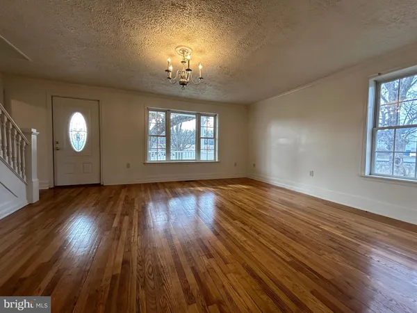 an empty room with wooden floor chandelier and windows