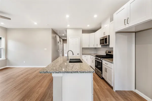 a kitchen with kitchen island granite countertop a stove top oven a sink dishwasher and a refrigerator with wooden floor