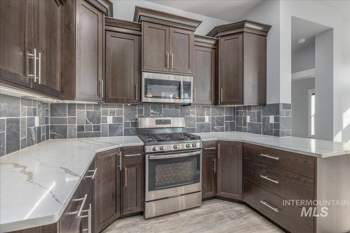 3036 Northwest 13th Street Meridian, ID 83646 - Photo 11 of 50 Kitchen featuring stainless steel appliances, dark wood finish cabinets, tasteful backsplash, light wood finished floors, and light stone counters