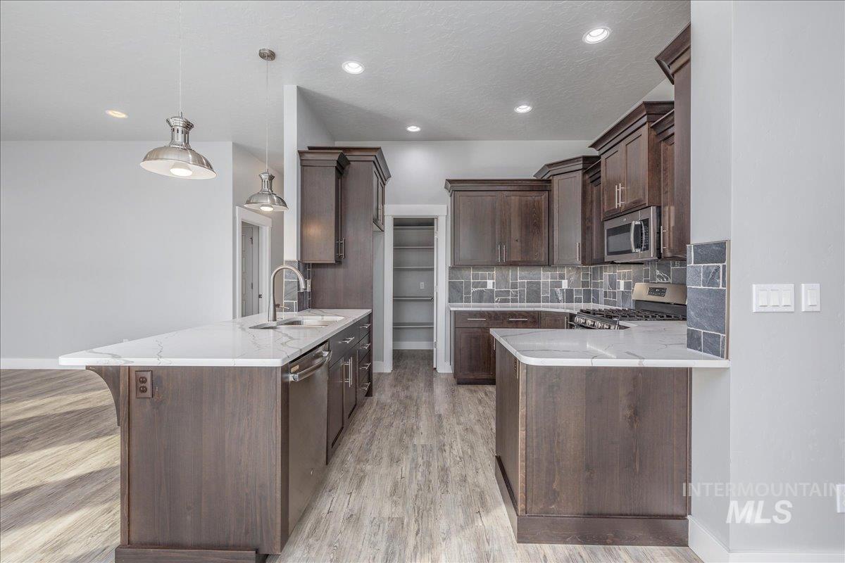 3036 Northwest 13th Street Meridian, ID 83646 - Photo 12 of 50 Kitchen featuring a peninsula, dark wood finish cabinetry, hanging light fixtures, stainless steel appliances, and light stone counters