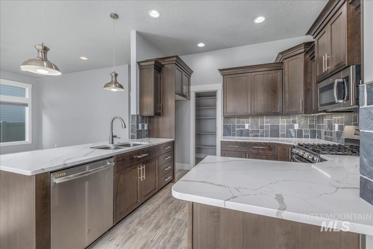 3036 Northwest 13th Street Meridian, ID 83646 - Photo 10 of 50 Kitchen with a peninsula, decorative backsplash, light stone countertops, stainless steel appliances, and dark wood finish cabinets