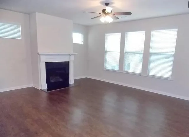 an empty room with windows fireplace and fan