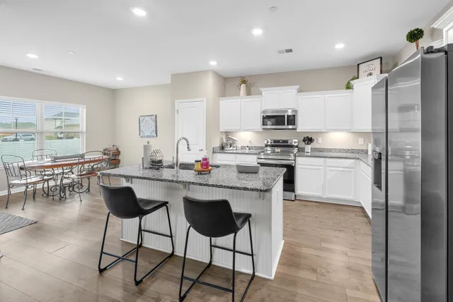 a kitchen with stainless steel appliances granite countertop a stove a sink a refrigerator and white cabinets with wooden floor