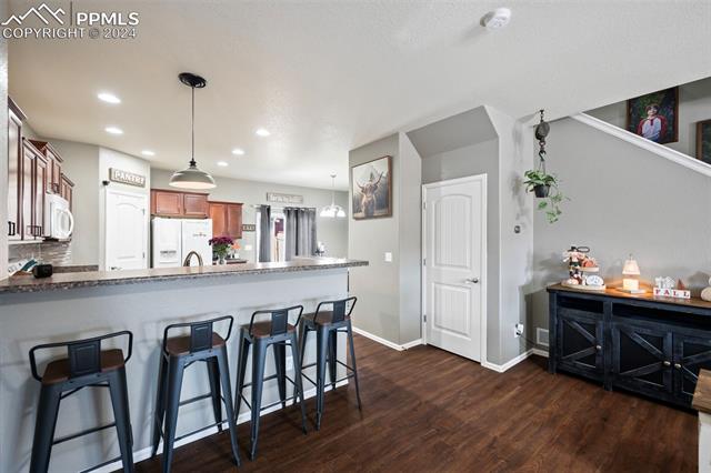 6382 Pilgrimage Road Colorado Springs, CO 80925 - Photo 11 of 32 Kitchen featuring dark wood-type flooring, kitchen peninsula, a kitchen bar, pendant lighting