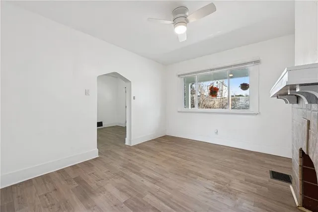 a view of an empty room with wooden floor and a ceiling fan