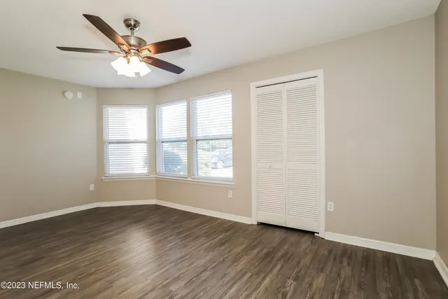 an empty room with wooden floor chandelier fan and windows