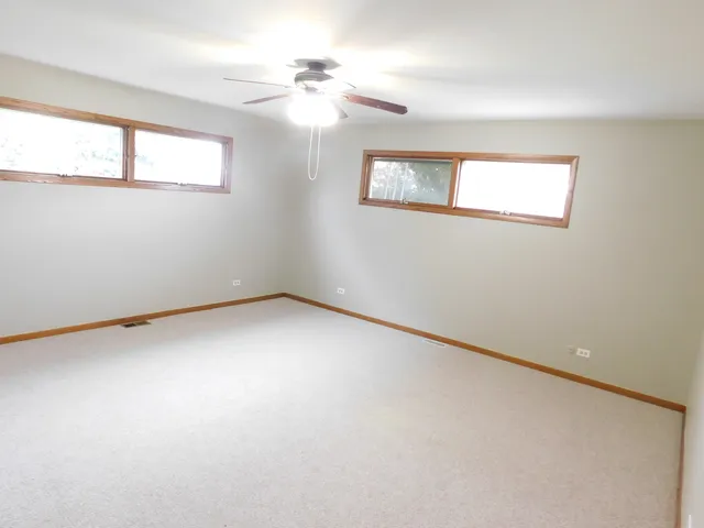 an empty room with chandelier fan and windows