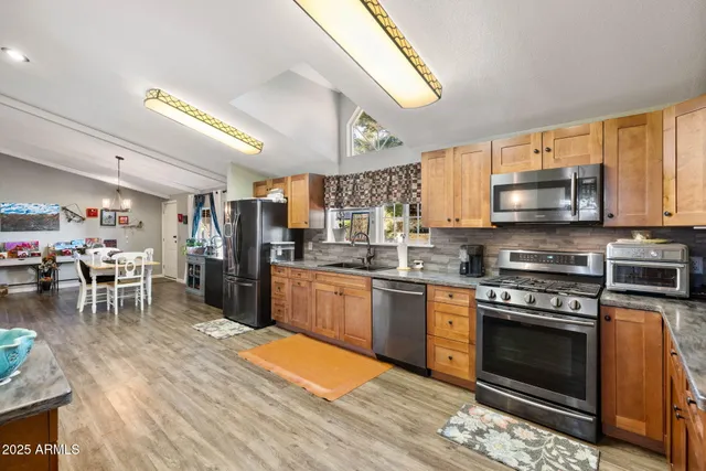 a kitchen with stainless steel appliances granite countertop a stove top oven a sink dishwasher a dining table and chairs with wooden floor