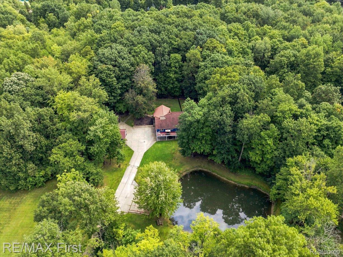 66200 Campground Road Washington, MI 48095 - Photo 47 of 62 Secluded property featuring a residence with a covered porch, a private pond, and a concrete driveway, surrounded by mature trees