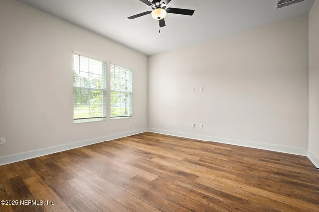 an empty room with wooden floor chandelier fan and windows