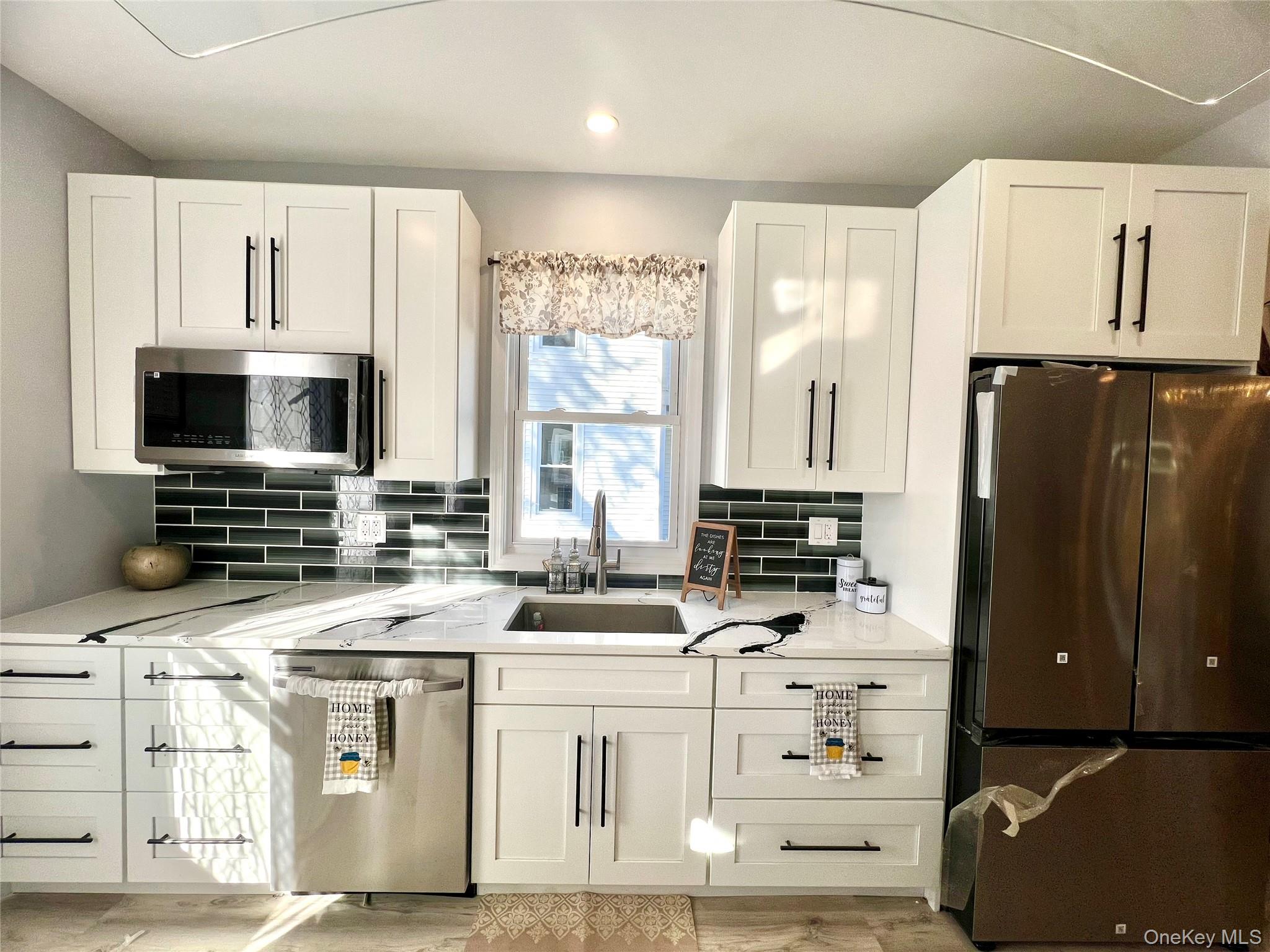 Kitchen featuring stainless steel appliances, white cabinetry, tasteful backsplash, light stone countertops, and recessed lighting