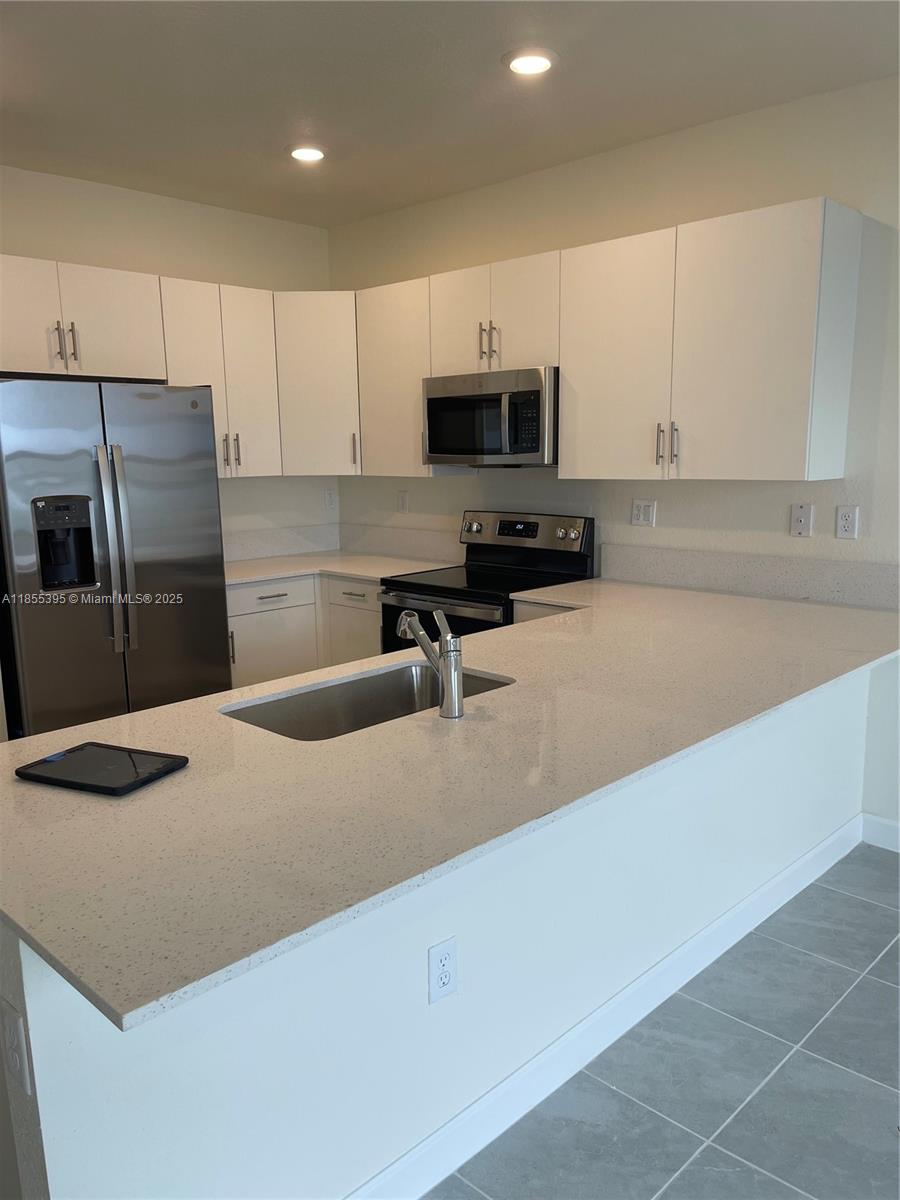 3244 West 114th Terrace, Unit 3244 Hialeah, FL 33018 - Photo 5 of 16 a kitchen with stainless steel appliances granite countertop a sink a stove top oven a refrigerator and white cabinets