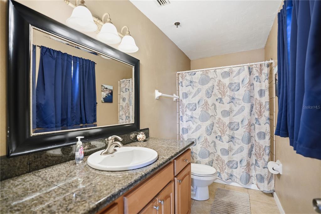 16330 Gulf Boulevard, Unit 306 Redington Beach, FL 33708 - Photo 23 of 39 a bathroom with a granite countertop sink toilet a mirror and shower curtain