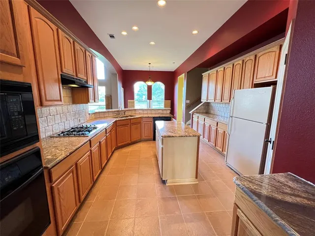 a large kitchen with stainless steel appliances granite countertop a stove top oven a sink and a refrigerator