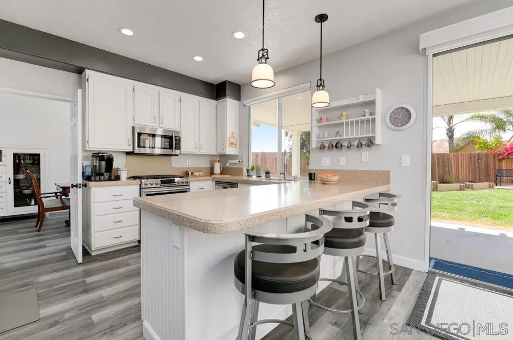 963 Martinique Drive Chula Vista, CA 91913 - Photo 15 of 37 a kitchen with kitchen island granite countertop a sink a stove a refrigerator cabinets and a dining table with wooden floor