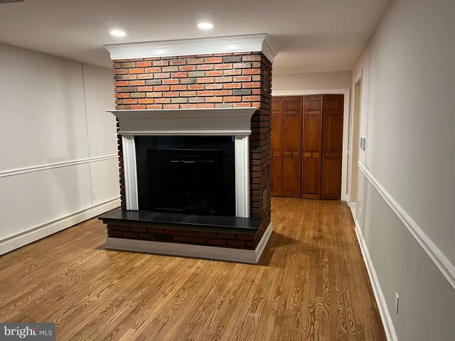 a view of an empty room with wooden floor a fireplace and a window