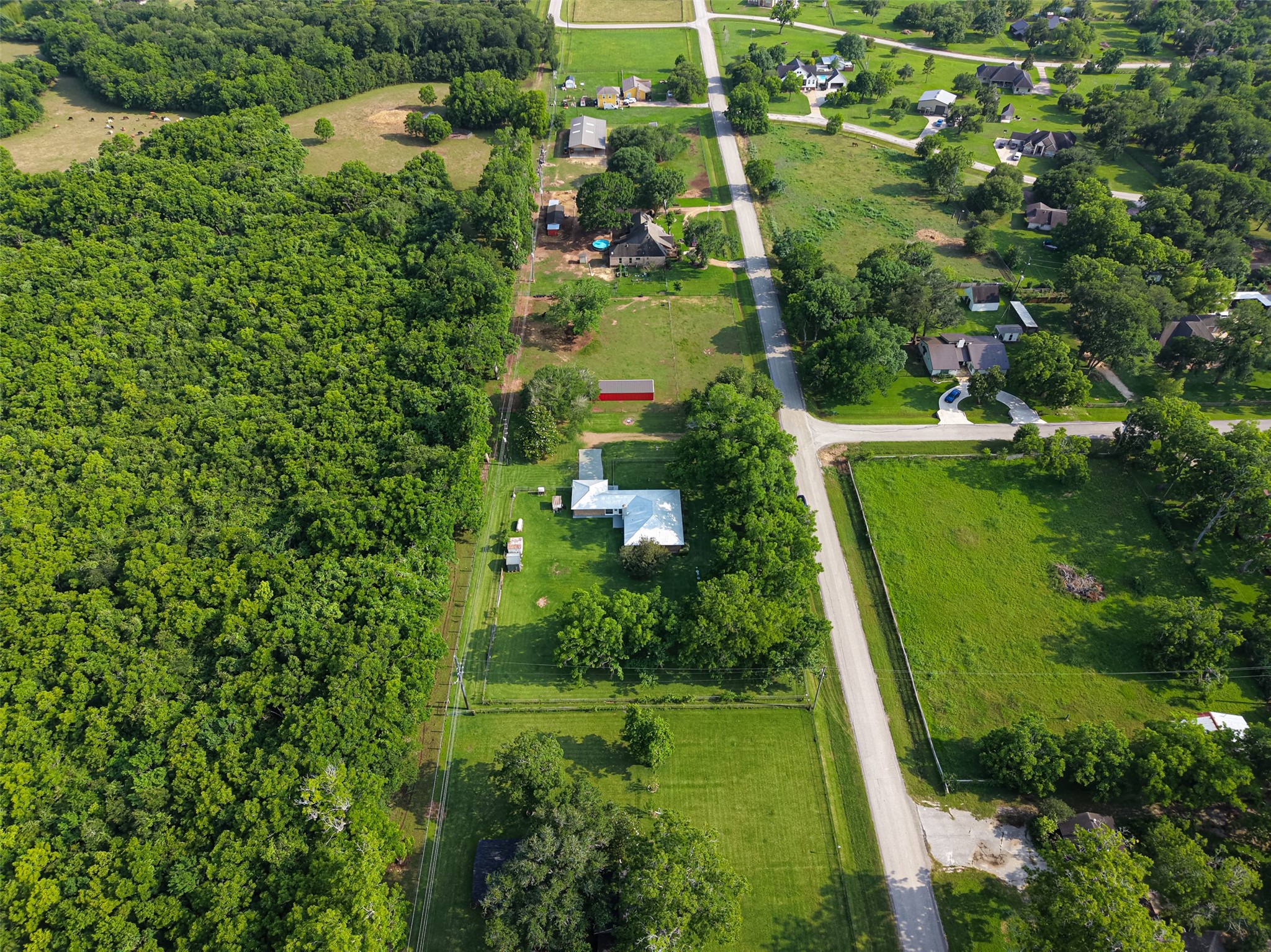 1004 Wagon Road Simonton, TX 77485 - Photo 38 of 40 This bird's-eye aerial view showcases the property's impressive lot size and its peaceful semi-rural setting, surrounded by lush greenery and open land. The home's distinctive metal roof stands out against the vibrant landscape, with ample yard space visible on all sides. The quiet road frontage and neighboring properties give a true sense of the open, unhurried lifestyle this location offers.