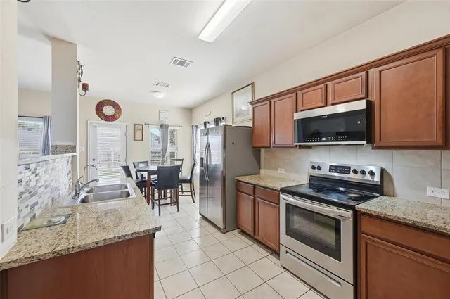 a kitchen with stainless steel appliances granite countertop a stove top oven a sink a dining table and chairs with wooden floor