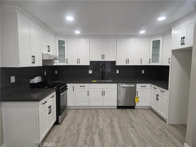 a kitchen with stainless steel appliances granite countertop a stove a sink a refrigerator and white cabinets