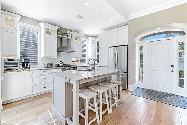 a kitchen with stainless steel appliances granite countertop a refrigerator a sink dishwasher a stove and white cabinets with wooden floor