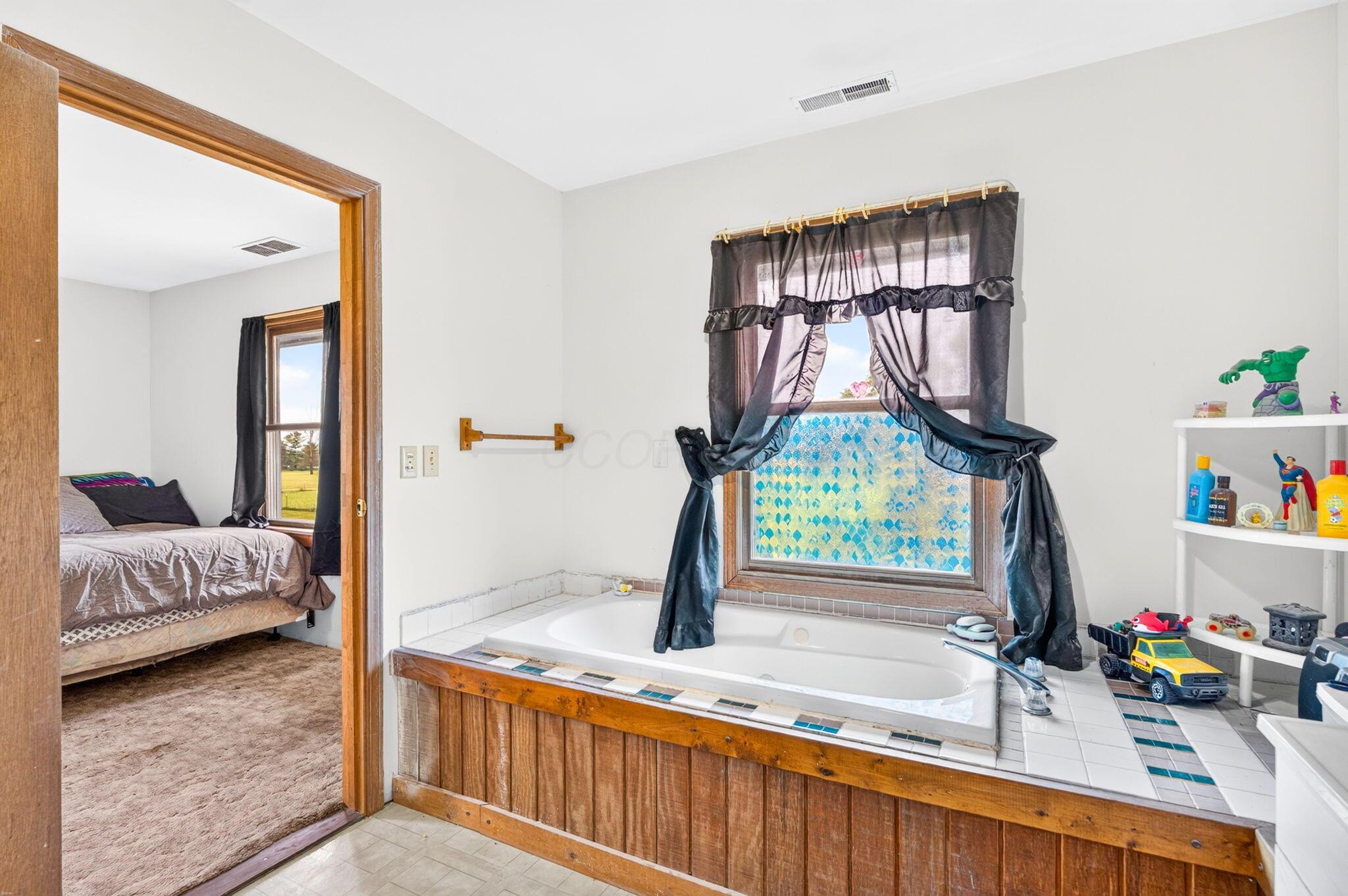 4780 North Section Line Road Radnor, OH 43066 - Photo 46 of 79 Built-in tub with wood paneling and tile surround, accompanied by a window with wood trim