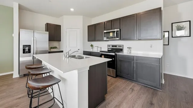 a kitchen with stainless steel appliances a sink a stove a refrigerator cabinets and a dining table