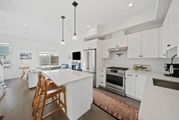 a kitchen with stainless steel appliances kitchen island granite countertop a stove a sink a refrigerator a dining table and chairs with wooden floor