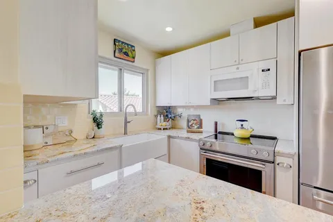 a kitchen with stainless steel appliances kitchen island granite countertop a sink dishwasher stove and white cabinets with wooden floor