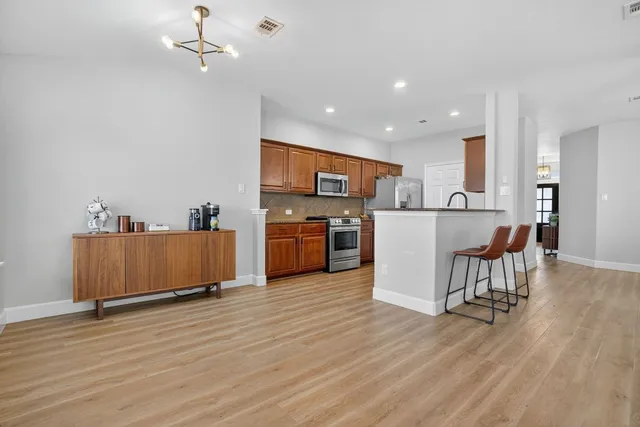 a view of kitchen with stainless steel appliances granite countertop a stove top oven a refrigerator a dining table and chairs with wooden floor