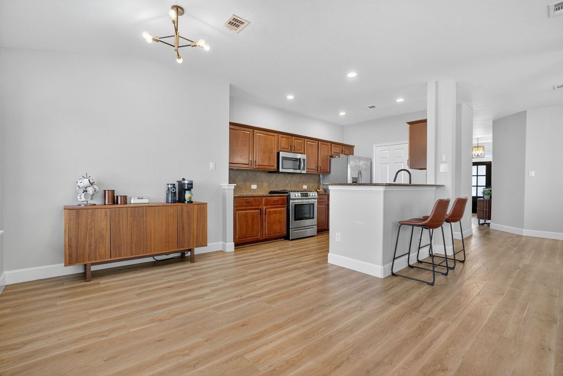 394 Verano Drive Kyle, TX 78640 - Photo 7 of 25 a view of kitchen with stainless steel appliances granite countertop a stove top oven a refrigerator a dining table and chairs with wooden floor