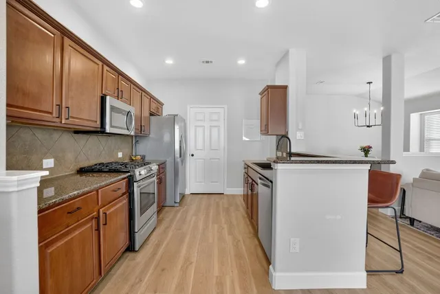 a kitchen with stainless steel appliances granite countertop a stove top oven a sink dishwasher and a refrigerator with wooden floor