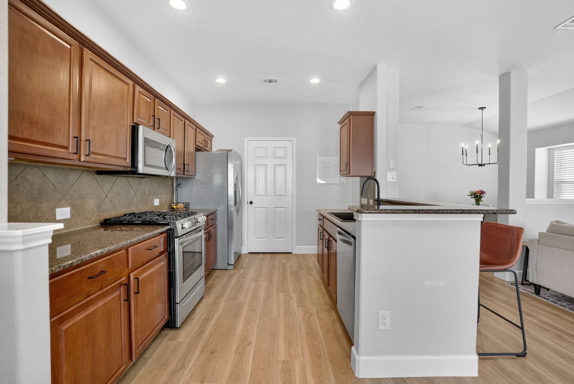 394 Verano Drive Kyle, TX 78640 - Photo 8 of 25 a kitchen with stainless steel appliances granite countertop a stove top oven a sink dishwasher and a refrigerator with wooden floor