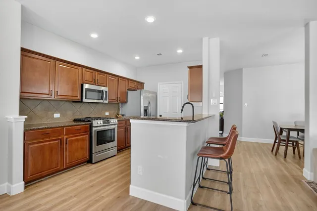 a kitchen with stainless steel appliances granite countertop a stove top oven a sink a dining table and chairs with wooden floor