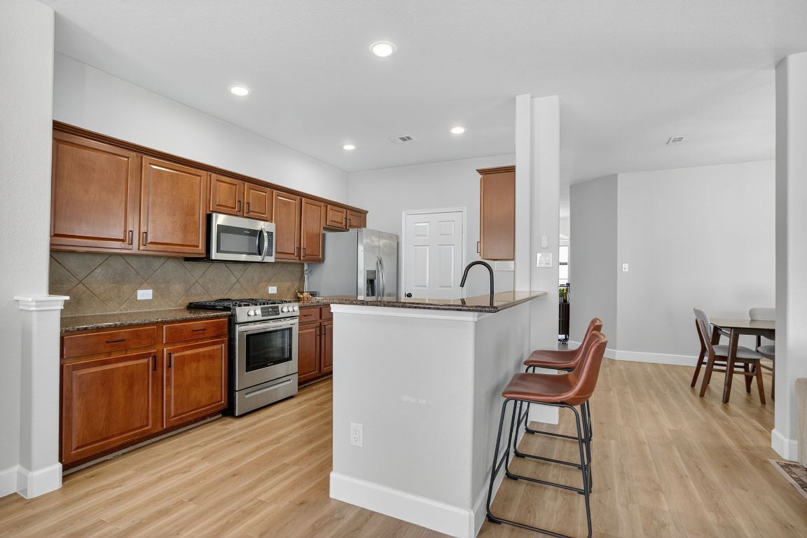 394 Verano Drive Kyle, TX 78640 - Photo 9 of 25 a kitchen with stainless steel appliances granite countertop a stove top oven a sink a dining table and chairs with wooden floor