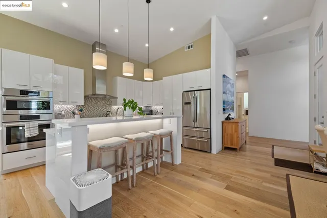 a kitchen with stainless steel appliances kitchen island granite countertop a refrigerator a stove a microwave oven a dining table and chairs with wooden floor