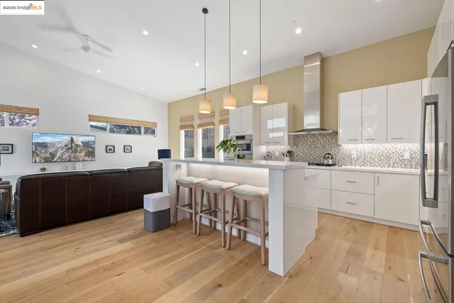 a kitchen with stainless steel appliances kitchen island granite countertop a refrigerator a stove a sink and white cabinets with wooden floor