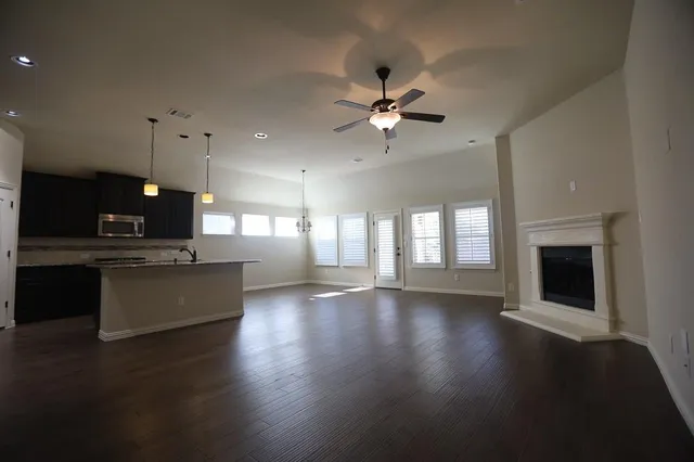 a view of an empty room with wooden floor and a kitchen