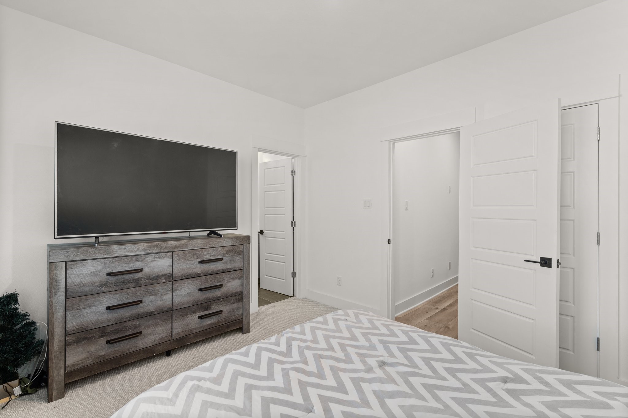 2928 Stevens Street Houston, TX 77026 - Photo 20 of 30 This bedroom features clean white walls, a chevron-patterned bedspread, and a dark wooden dresser with a large TV. It offers ample storage with a closet and contemporary white doors.