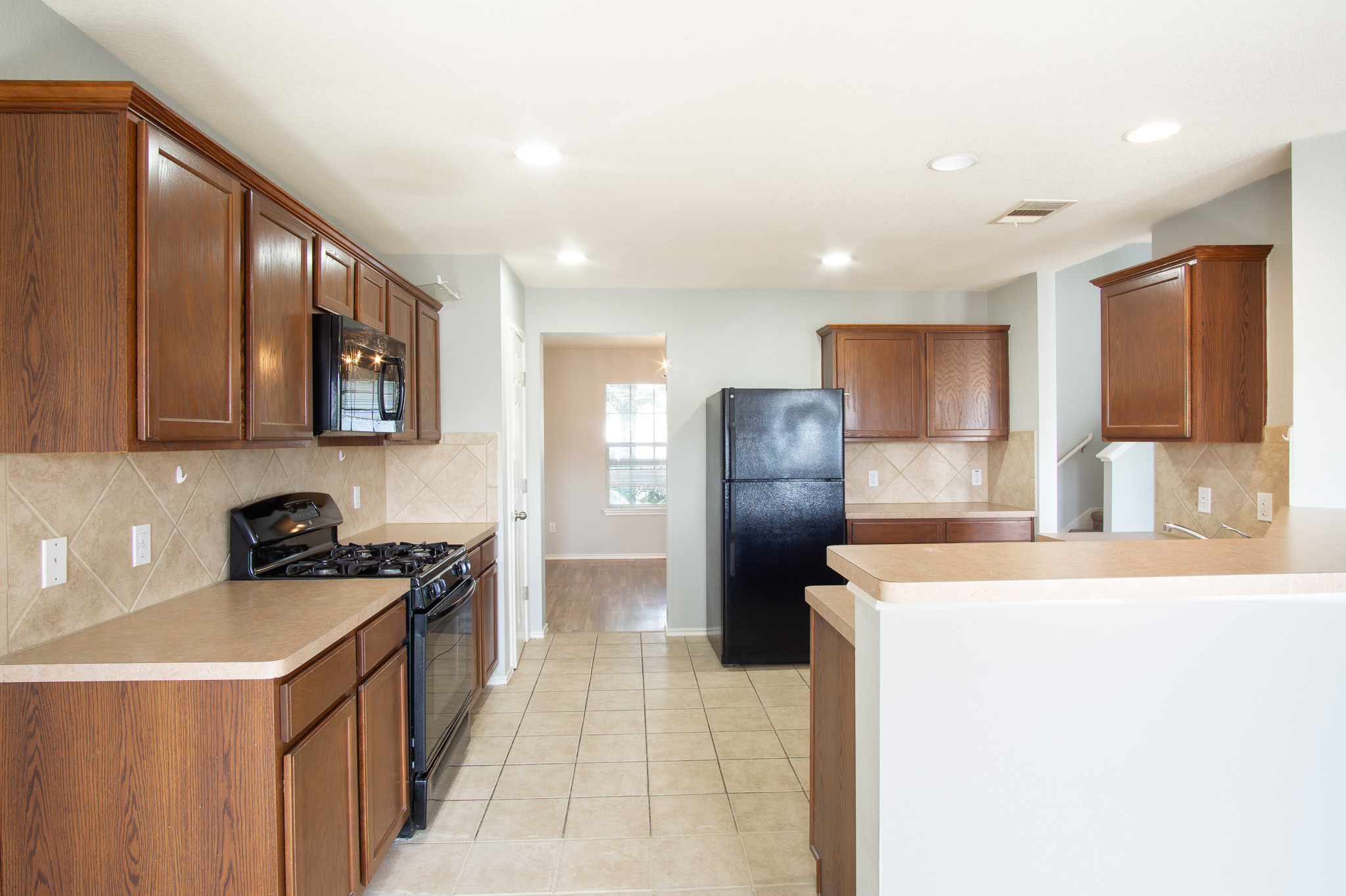 210 King Ridge Drive Buda, TX 78610 - Photo 7 of 29 Kitchen featuring black appliances, tasteful backsplash, light countertops, wood finish cabinets, and a peninsula