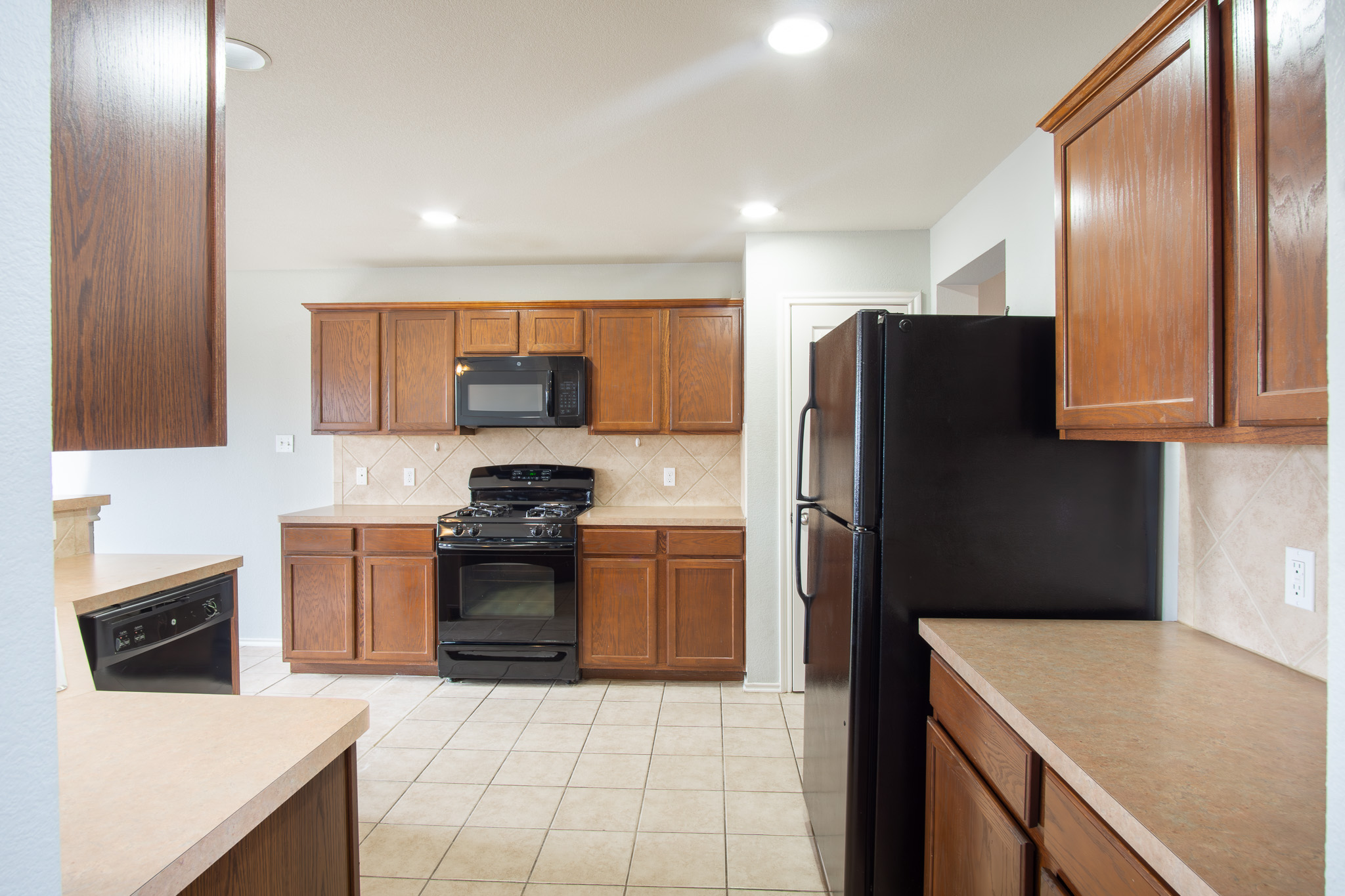 210 King Ridge Drive Buda, TX 78610 - Photo 8 of 29 Kitchen with wood finish cabinetry, black appliances, light countertops, light tile patterned floors, and backsplash