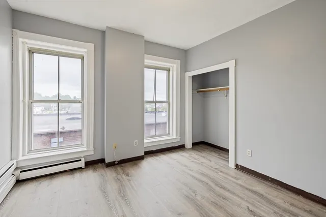 an empty room with wooden floor closet and windows