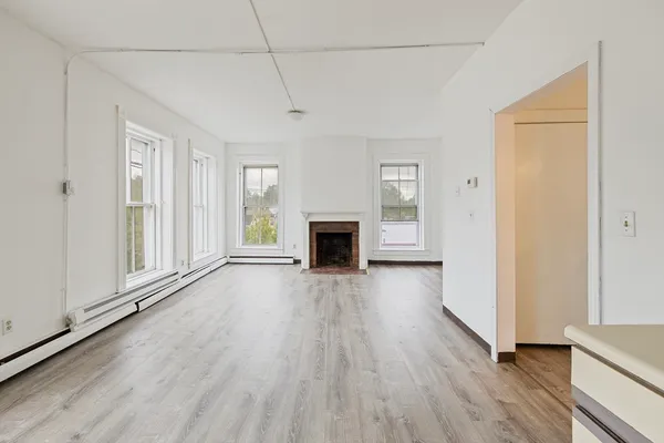 an empty room with wooden floor fireplace and windows