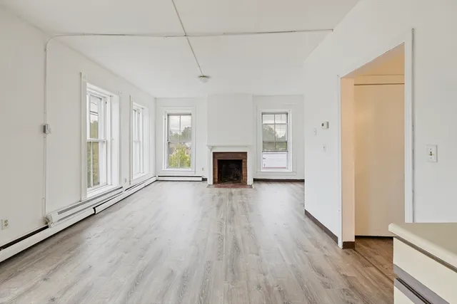 an empty room with wooden floor fireplace and windows