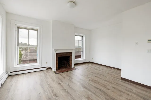 an empty room with wooden floor fireplace and windows